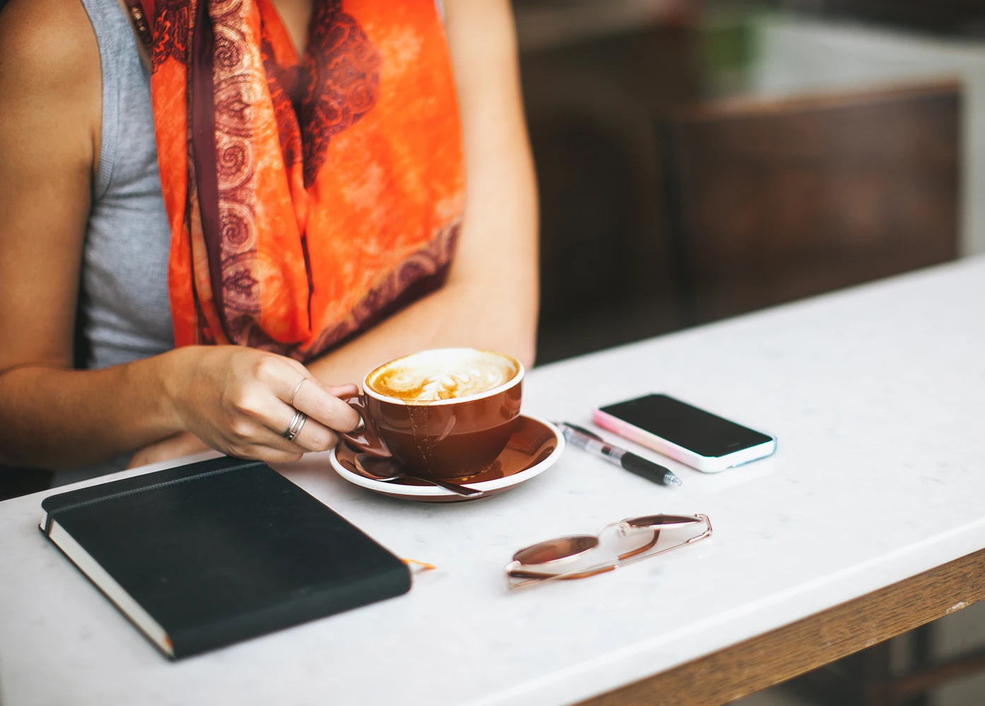Person holding a latte at a café table with notebook and phone